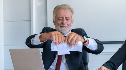 aggressive Senior businessman are throwing paper on around desk office. with young afraid...
