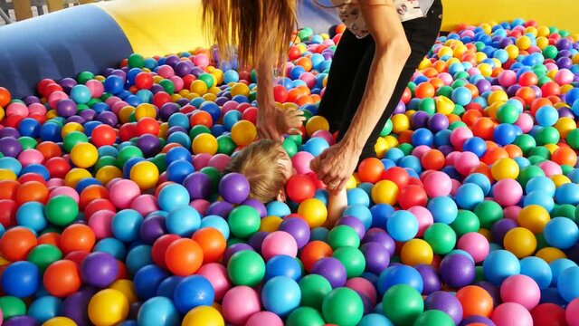 A young beautiful woman and her little son have a fun in the pool of colorful balls