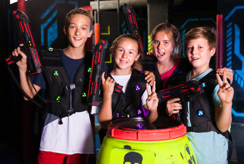 Fototapeta na wymiar Group portrait of happy teenagers with laser guns having fun on dark lasertag arena..