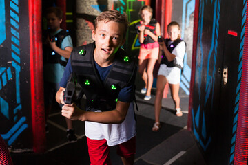 Obraz na płótnie Canvas Excited boy aiming laser gun at other players during lasertag game in dark room..