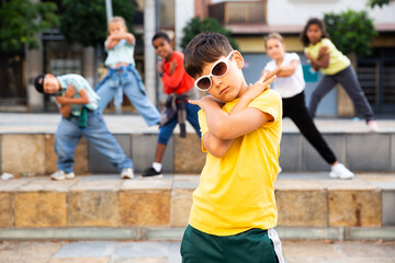 Confident tween boy hip hop dancer posing while performing with group on summer city street.