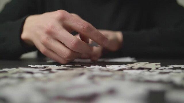 Puzzle pices falling on a table with a person's hands trying to solve the puzzle in the background. Shot in 4K, Slow Motion with Shallow Depth of Field.