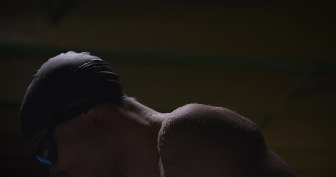 Cinematic close up shot of young professional male swimmer with cap and goggles is warming up and breathing deeply while practicing training in swimming pool. Concept of sport, competition, victory.