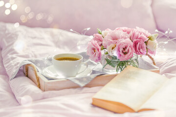 Wooden tray with a cup of coffee, book and pink lisianthus flowers, romantic and relax concept. Breakfast in bed. Selective focus