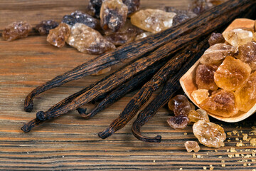 Crystals of brown sugar in a wooden scoop with vanilla beans on a wooden background.