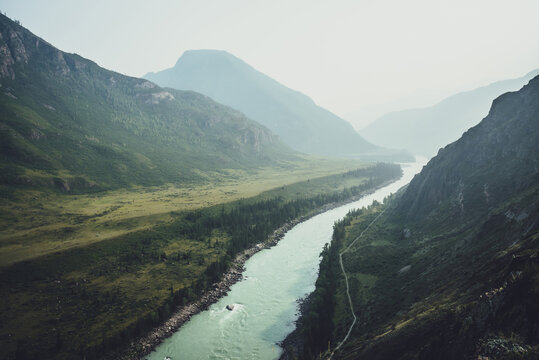 Misty mountain landscape with wide mountain river. Dark green gloomy scenery with confluence of two mountain river in mist. Dark atmospheric view to confluence of great rivers in rainy weather. © Daniil