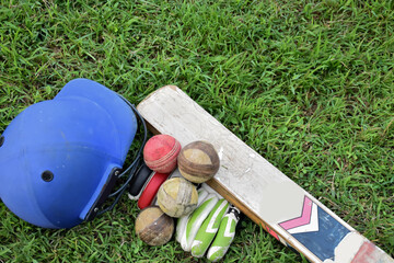 Old leather cricket ball and cricket sportwears on the green grass court, concept for practicing cricket sport after school of Asian students. 