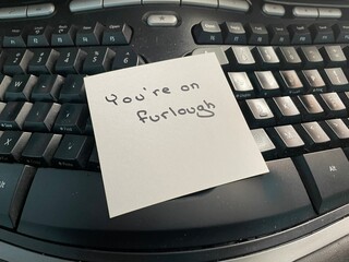A handwritten note on a computer keyboard stating you’re on furlough. Furlough is a leave of...