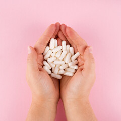 Hands hold pills isolated on pastel coloured background. Medication and prescription pills flat lay...