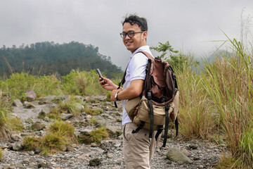 Young asian backpacker man is happy and smile when he looking smartphone in mountain traveling