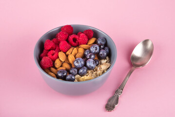 Healthy breakfast bowl: oatmeal with raspberry, almond, blueberries and chia seeds. Rustic spoon. pink pastel background