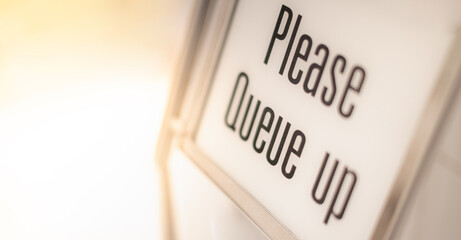 Due to Coronavirus disease COVID-19,  PLEASE QUEUE  Sign at new normal pandemic and social distancing Covid-19 in supermarket entrance with blur background.