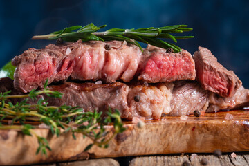 Close-up of delicious beef steak on wooden kitchen table, with rosemary.Blue background, meat sale - banner