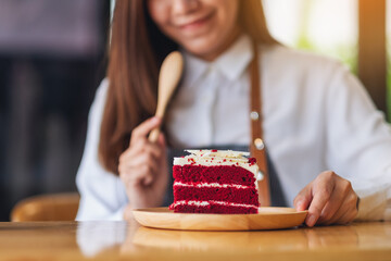 Closeup image of a beautiful woman, female chef baking and eating a piece of red velvet cake in wooden tray