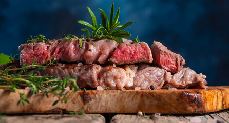 Close-up of delicious beef steak on a wooden table, still life. Rare steak. Dark blue background, cooking and recipe book, cooking steaks