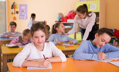 Girl and group children 9-10 years old at lesson, woman teacher helping to ...