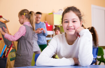 Portrait of smiling schoolgirl sitting at table in classroom relaxing during break