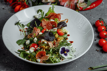 salad with ham and pear on dark gray background. jamon salad, salad mix, spinach, pear, cherry tomatoes, Dor Blue, capers and vinegar dressing Bianco