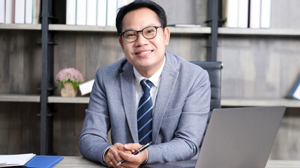 Portrait of senior asian businessman smiling and looking at camera while sitting at office,...