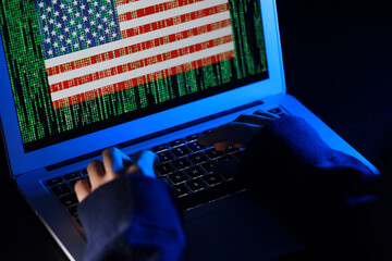 A hacker with computer hacking and stealing data information, Selective focus image, Flag of the United States and binary code as background, cybersecurity concept.