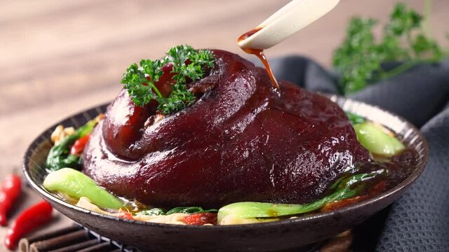 Pouring savory soy sauce with spoon over Taiwanese braised pork hock food in a plate.