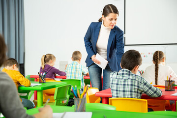 Positive boys and girls studying and female teacher helping in classroom. High quality photo