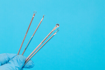 Doctor's hand in a blue glove holds a set of tools for Acne removal.