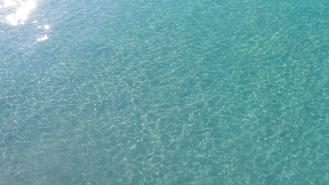 Cystal clear cyan blue sea water surface n calm ocean wave or ripple with bright shining sun glare n sunlight ray flare in tropical summer or spring sunshine day, 4k cinemagraphs b-roll footage video