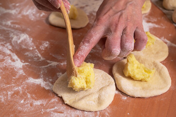 A woman puts the mashed potato stuffing on small dough cakes. Homemade baking
