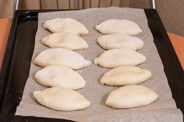 On a baking sheet are raw Russian dough pies with filling. Homemade baking
