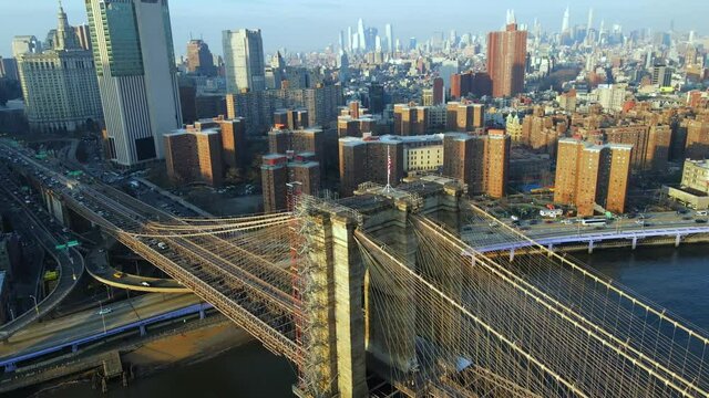 Cinematic aerial overlooking Brooklyn Bridge and tilting up revealing stunning Manhattan skyline and buildings on sunny summer day in New York City, USA.