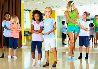 Group of positive smiling children practicing vigorous jive movements in dance class with female...