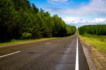 Fototapeta na wymiar An asphalt road outside the city, after the last rain. Intercity deserted track passing through a summer forest.