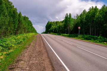 An asphalted intercity road with white markings extending into the distance through a green forest.