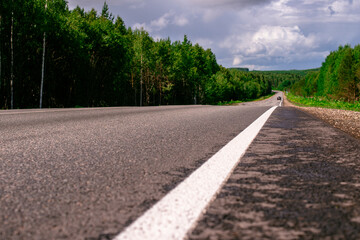 An asphalted intercity road with white markings extending into the distance through a green forest.