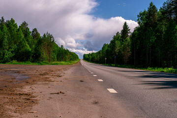 Fototapeta na wymiar An asphalted intercity road with white markings extending into the distance through a green forest.