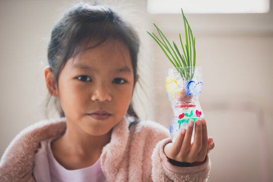 Asian child girl showing her recycle flower pot after finish painting on plastic bottle with watercolor. Kids arts and crafts creative activity in home during quarantine due to Covid 19 pandemic.