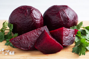 Boiled beets whole and cut on a cutting Board with parsley leaves on a white background. Copy space