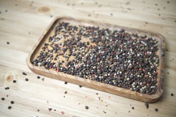 A mixture of Indian seasonings is poured into a wooden plate on a wooden table. Black pink pepper. Ingredients for the dish