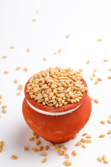 Wheat grains in clay pot on white background
