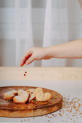 Heart-shaped cookies on round wooden cutting board. Saint Valentine's cookies in shape of heart. Hand pouring out golden glitters in shape of heart on white background.