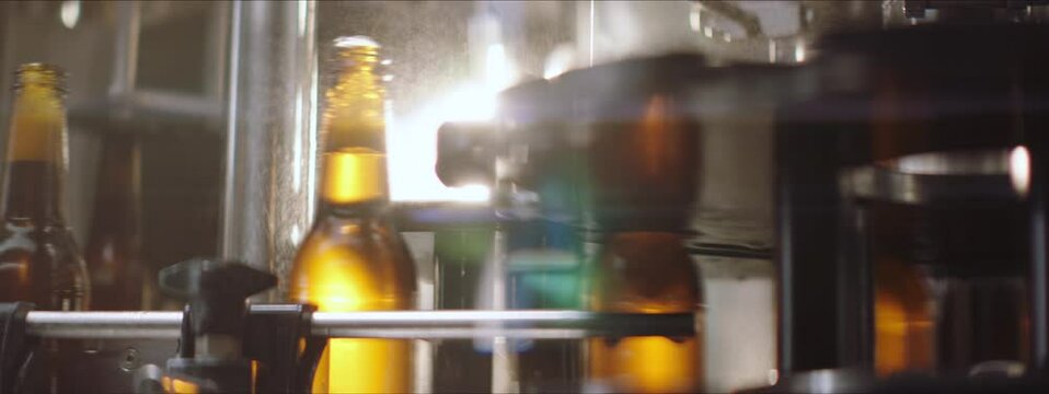 Filled beer bottles moving on a conveyor belt in a factory. Close-up video of beer bottles on a modern machine. Splashes of water. Brewery, factory concept.