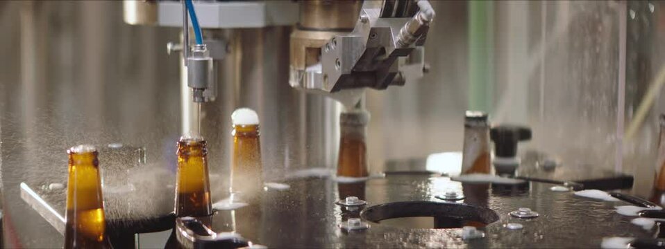 Foam overflowing beer bottles in a process of brewing. Beer bottles moving on a modern machine and getting closed. Capping process of glass bottles. Factory, brewery concept.