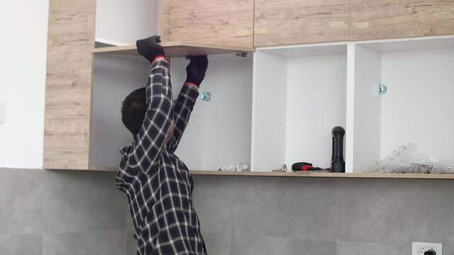 The carpenter screwing in and mounting hinge on kitchen shelves.