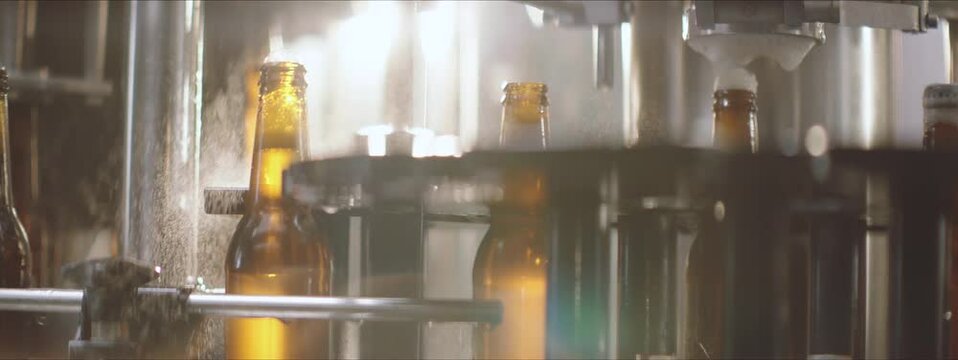 Production of beer in a brewery. Glass bottles moving along the conveyor belt. Capping process of full beer bottles. Factory, brewery concept.