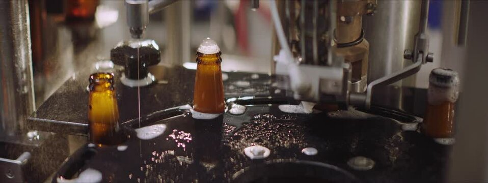 Video of a modern machine closing glass beer bottles. Full beer bottles moving on a industrial machinery. Factory, brewery concept.