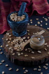Peanuts in a marble bowl, peanut butter in a jar and a wooden spoon on a parota board.