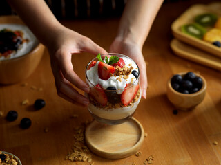 Female serving a glass of granola with Greek yogurt and fresh berries on wooden table