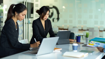 Two businesswomen working together in glass partition meeting room
