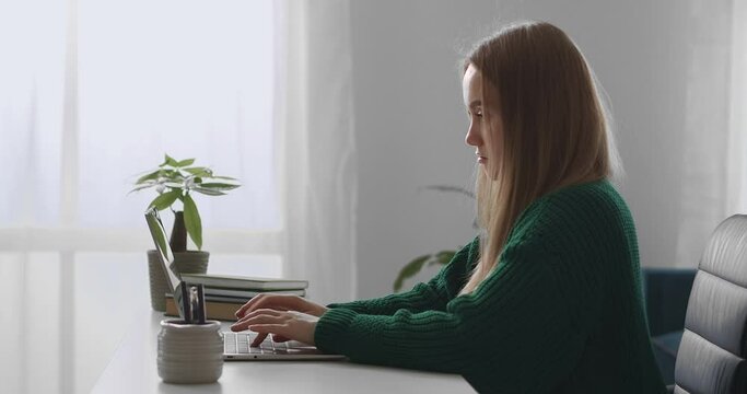 freelancer woman is typing message in laptop, sitting at table in home office, internet work from home